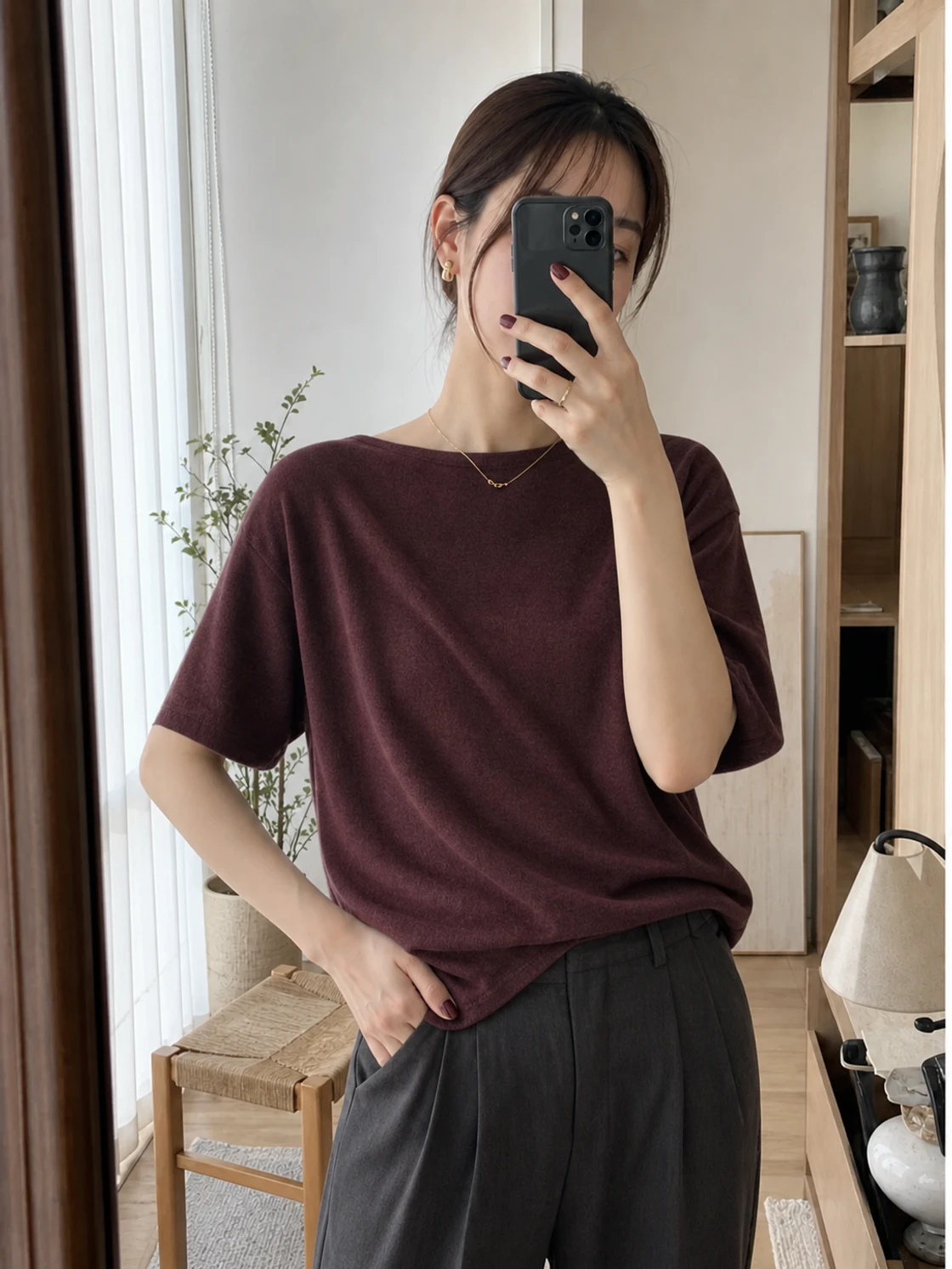 スマートフォンを持って服とアクセサリーを試す鏡越しの半身写真